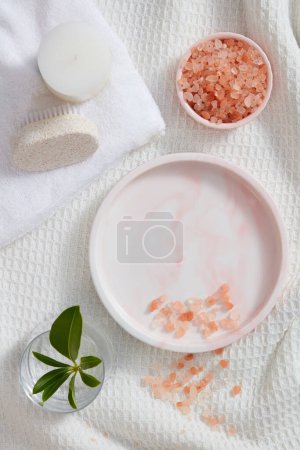 Photo for Flat lay of a bowl containing pink himalayan salt displayed with a foot brush and white candle. Vacant space on marble tray to show product. Pink himalayan salt is a natural skincare ingredients - Royalty Free Image