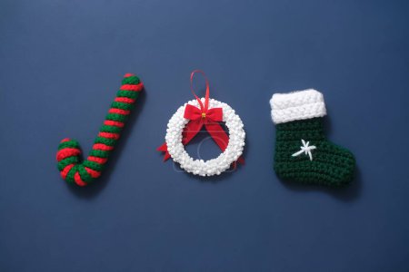 Photo for Top view of cute woolen accessories to decorate pine tree at Christmas: candy cane, stocking and lovely laurel wreath on dark blue background - Royalty Free Image