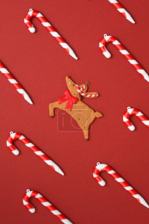 Photo for Flat lay composition with Christmas candy canes and cute reindeer shaped cake decorated on a red background. Creative photo for advertising. Christmas is the celebration of the birth of Jesus - Royalty Free Image