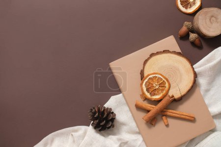 Photo for Design Christmas holiday photos in a minimalist style. Light brown notebook, oak veneer, wooden podium and cinnamon stick decorated with white cloth on dark brown background. Top view, copy space - Royalty Free Image