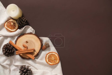Foto de Diseño navideño en estilo minimalista. Sobre un fondo marrón cálido, una plataforma de madera, conos de pino secos y palitos de canela se colocan sobre una llamativa toalla blanca. Espacio para texto y diseño - Imagen libre de derechos