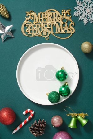 Foto de Fondo creativo para la publicidad y el producto de marca con el concepto de vacaciones de Navidad. Decoraciones coloridas como adornos, campanas, bastones de caramelo que se muestran en el fondo verde con plato de cerámica blanca - Imagen libre de derechos