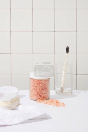 Photo for Transparent jar of pink himalayan salt without label decorated with a brush and towel. A brush displayed inside a glass. Product promotion with unlabeled jar - Royalty Free Image