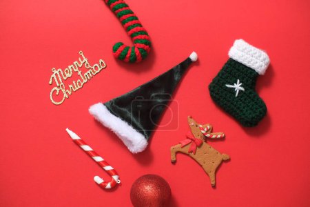 Foto de Algunos objetos decorativos lindos con muchos significados para la Navidad se muestran sobre un fondo rojo. Sombreros y stock de Santa Claus, renos, bastón de caramelo y Feliz Navidad deseos - Imagen libre de derechos
