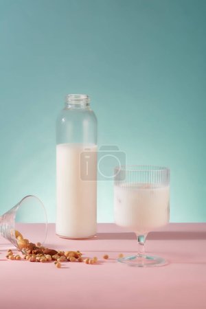Foto de Botella transparente y taza llena de leche de soja decorada con mucha soja sobre fondo azul. La leche de soja está llena de compuestos vegetales - Imagen libre de derechos