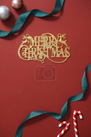 Téléchargez les photos : Carte de vœux de Noël avec des boules, des cannes à bonbons et un ruban vert sur fond rouge. Joyeux vœux de Noël au milieu et espace vide pour le design - en image libre de droit
