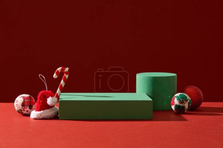 Photo for Abstract background for branding and minimal presentation with Xmas concept. Cute candy canes, woolen hat and baubles decorated with green podiums on red background - Royalty Free Image