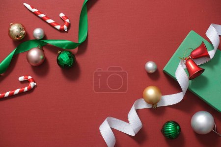 Photo for Top view of cute baubles, candy canes, bells and green ribbons decorated on red background. Christmas holiday concept. Minimal art background with copy space for design. Flat lay - Royalty Free Image