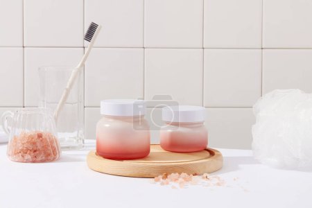 Foto de Dos frascos vacíos colocados en el podio de madera. Una taza que contiene sal rosa himalaya y una taza con cepillo de dientes. concepto de cuidado suave de la piel - Imagen libre de derechos