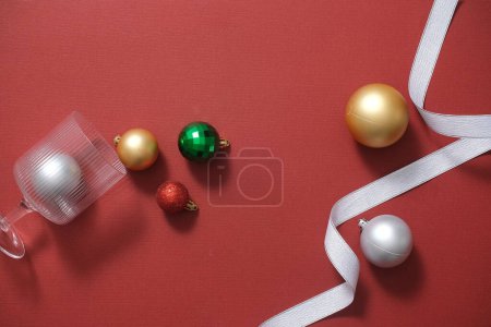 Foto de Fondo navideño con adornos coloridos, copa de vidrio y cinta sobre fondo rojo. Vista superior. Marco para la tarjeta de Navidad de diseño o producto de la exhibición - Imagen libre de derechos