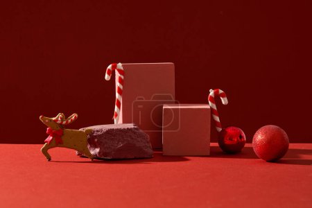 Foto de Concepto minimalista para la publicidad con el tema de Navidad. Sobre un fondo rojo, bastones de caramelo, chucherías y lindos renos decorados con podios. Espacio en blanco para el producto y el diseño de la pantalla - Imagen libre de derechos