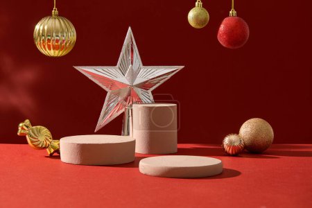Photo for Christmas concept with blank space for presentation product. Cute baubles and star displayed on red background with cylinder podiums. Front view, advertising photo - Royalty Free Image