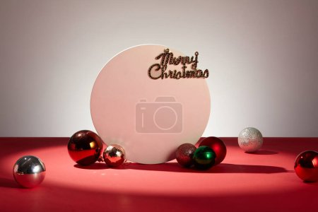 Foto de Hermosas y coloridas bolas de Navidad están decoradas con un podio blanco redondo y las palabras Feliz Navidad sobre un fondo rojo. Escenario iluminación destaca ubicaciones de visualización del producto - Imagen libre de derechos