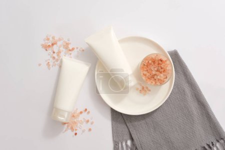 Foto de Bufanda gris decorada con dos tubos blancos sin etiqueta y un tazón de sal de color rosa himalaya. Vista superior. Etiqueta vacía para publicidad de productos de belleza natural - Imagen libre de derechos