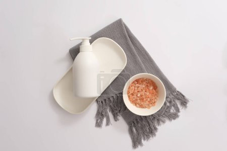 Photo for Ceramic bowl containing pink himalayan salt and blank label pump bottle decorated on a gray scarf. Some claim that Himalayan salt is more natural than table salt - Royalty Free Image