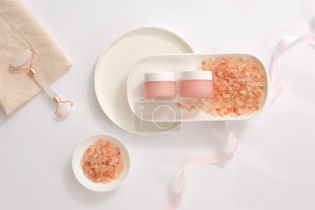 Foto de Plato blanco con una pila de sal de color rosa himalaya y dos frascos sin marca en color rosa. Cosméticos, productos para el cuidado y concepto de higiene personal - Imagen libre de derechos