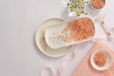 Photo for Pink himalayan salt divided on many different plates, decorated with pink ribbon, flowers pot and facial massage roller. Blank space for text adding - Royalty Free Image