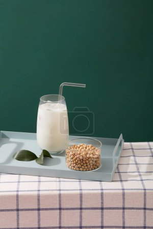 Photo for A tray in pastel color featured a milk cup with straw and a transparent bowl of soybeans. Green background. Soy milk is a well-known dairy milk replacement - Royalty Free Image