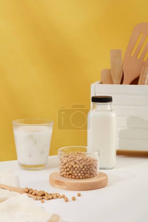 Téléchargez les photos : Bol transparent de soja mis sur un podium en bois, affiché avec une tasse et une bouteille de lait. Vue de face. La protéine dans le lait de soja est saine - en image libre de droit