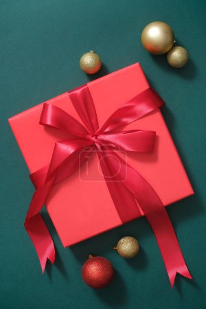 Photo for A red gift box stand out with red ribbon tied into a lovely bow shape, decorated with some baubles on a green background. Christmas photography with lovely decorations - Royalty Free Image