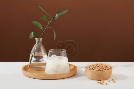 Foto de Maceta de vidrio de hojas verdes decorada con una taza de leche y un tazón de madera de soja. La mayoría de la leche de soja que se encuentra en los supermercados está fortificada con nutrientes añadidos - Imagen libre de derechos