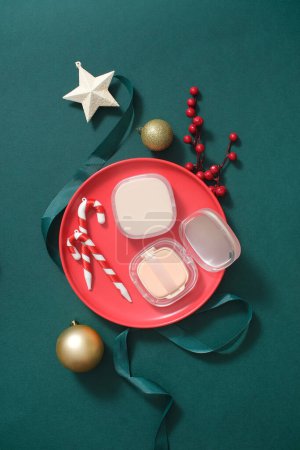 Photo for On a red ceramic dish, an unbranded cushion box displayed, decorated with candy canes, star, bauble and ribbon. Top view, scene for advertising cosmetic product with Christmas holiday concept - Royalty Free Image