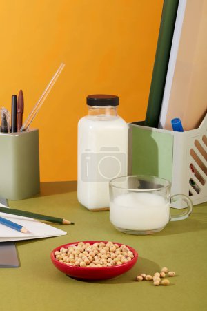 Photo for Blank label bottle of milk displayed on an office desk with a milk cup and a red dish of soybeans. Organic product advertising with empty label - Royalty Free Image