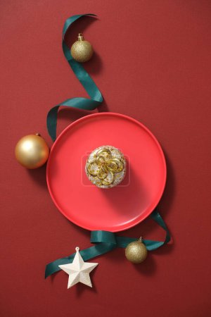 Photo for Top view of red ceramic dish decorated with some cute objects such as star, baubles and green ribbon stand out. Space for presentation product. Minimalist concept, Christmas holiday - Royalty Free Image
