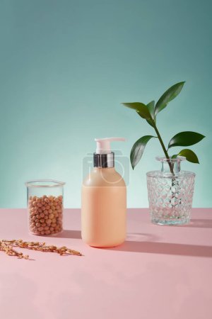 Photo for Unlabeled pump bottle in yellow color decorated with a beaker of soybeans against blue background. Cosmetic product advertising with empty label - Royalty Free Image