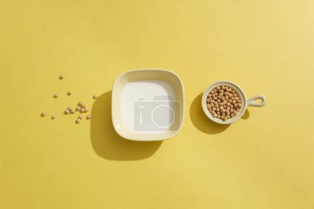 Foto de Cuencos de cerámica que contienen leche fresca y un montón de soja sobre fondo amarillo. Comer alimentos a base de soja puede reducir el riesgo de varios problemas de salud. - Imagen libre de derechos
