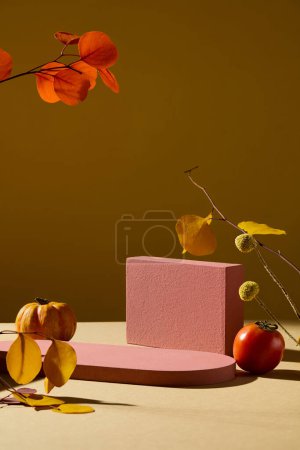 Foto de Plataforma vacía para presentación de cosméticos. Mockup con geometrías rojas podios decorados con calabaza, tomate y hojas secas de otoño sobre fondo marrón - Imagen libre de derechos
