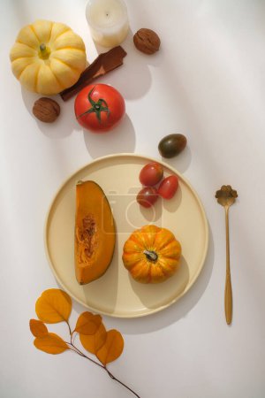 Photo for Ideas for party decorations for Thanksgiving. Ceramic plate containing pumpkins, decorated with ripe tomatoes, cinnamon and walnuts on white background. Vertical frame for social network advertising - Royalty Free Image
