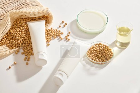 Photo for Blank label tubes in white color displayed with a mesh bag of soybeans and glassware filled with milk and oil. Soybean is associated with reducing the visible effects of skin aging - Royalty Free Image