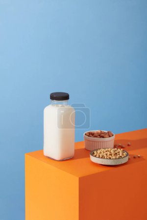 Photo for A podium in orange color featured bowls of peanuts and soybeans with unlabeled bottle of milk. Research shows that making nuts a regular part of a healthy diet helps to regulate our weight - Royalty Free Image