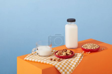 Foto de Platos rojos con varios tipos de frutos secos y frijoles arreglados con una botella de leche sin marca en el podio naranja. Todas las nueces tienen macronutrientes muy similares - Imagen libre de derechos
