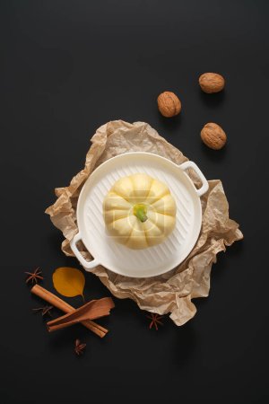 Photo for Pumpkin on ceramic pan decorated with beige paper, walnuts, cinnamon sticks and star anise on black background. Decorative frame for thanksgiving and halloween with minimalist concept - Royalty Free Image