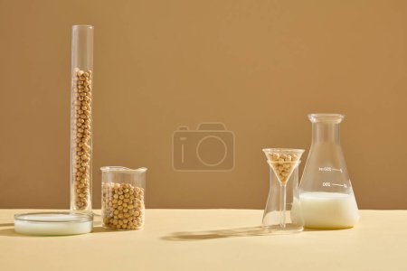 Foto de Sobre fondo beige, se muestran algunos artículos de vidrio que contienen semillas de soja y leche. Espacio vacío en el medio para la promoción de productos orgánicos - Imagen libre de derechos