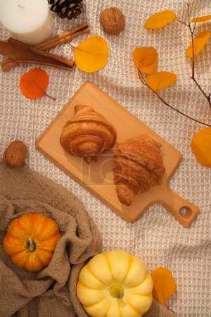Foto de Composición plana de otoño con deliciosos croissants en bandeja de madera, decorada con hojas secas y calabazas sobre fondo de tela vintage. Disfrute de un delicioso aperitivo otoñal - Imagen libre de derechos