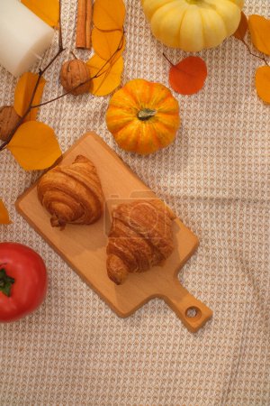 Foto de Fondo de tela con bandeja de madera de deliciosos cruasanes decorados con hojas de otoño, calabazas y nueces. Vista superior, espacio vacío para el diseño. Publicidad foto - Imagen libre de derechos