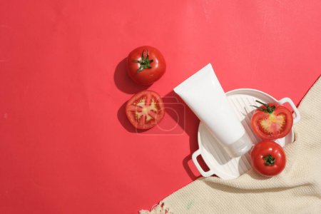 Photo for Against the red background, tomatoes cut in half are featured with unbranded tube. Tomatoes (Solanum lycopersicum) have many health and skin benefits - Royalty Free Image