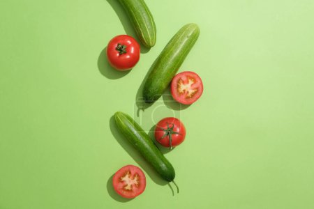 Photo for Green background featured fresh tomatoes cut in half and some cucumbers. The enzymes present in tomatoes help in gently exfoliating the skin - Royalty Free Image