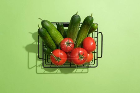 Téléchargez les photos : Panier contenant plusieurs concombres et tomates frais isolés sur fond vert. Vue de dessus. La tomate (Solanum lycopersicum) peut réduire le risque de dommages causés par le soleil - en image libre de droit