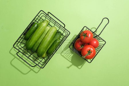 Foto de Los pepinos y los tomates se separan en dos cestas. Fondo verde. Usar tomate (Solanum lycopersicum) en la cara funciona como astringente - Imagen libre de derechos