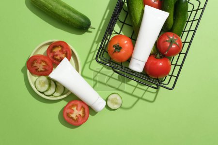 Photo for Two blank label tubes in white color displayed with a dish and a basket of tomatoes and cucumbers. Mockup of skin care cosmetic tube of beauty facial - Royalty Free Image