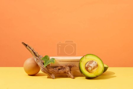 Photo for Scene for advertising cosmetic with blank space for presentation cosmetic product. Fresh halves of avocado decorated with dry twig and wooden podium on orange background. Front view - Royalty Free Image
