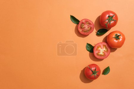 Téléchargez les photos : Fond orange avec quelques feuilles vertes et tomates coupées en deux. Espace vide pour montrer votre produit cosmétique extrait de Tomate (Solanum lycopersicum) - en image libre de droit