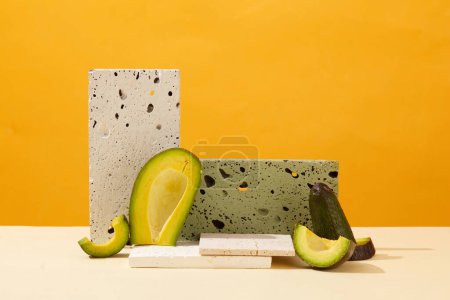 Photo for Minimalist background for presentation cosmetics with avocado extract. Fresh slices of avocado and gray bricks podiums decorated on yellow background. Front view - Royalty Free Image