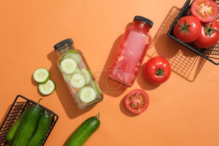 Téléchargez les photos : Deux bouteilles en verre de jus de tomate et d'eau de désintoxication au concombre affichées avec des paniers de tomates et de concombres. Le jus est bon pour la santé et aussi votre peau - en image libre de droit