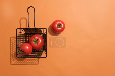 Foto de Escena mínima de una cesta negra que contiene tomates rojos sobre fondo naranja. El producto extraído de Tomate se puede mostrar en un espacio vacío - Imagen libre de derechos