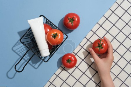 Téléchargez les photos : Un panier contenant des tomates et un tube d'étiquette vierge affiché. Modèle main tenant une tomate. Étiquette vierge beauté naturelle pour le concept de maquette de marque - en image libre de droit